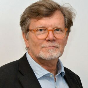 Middle aged white man with glasses, light brown to gray hair and beard. He wears a light blue shirt and black jacket.
