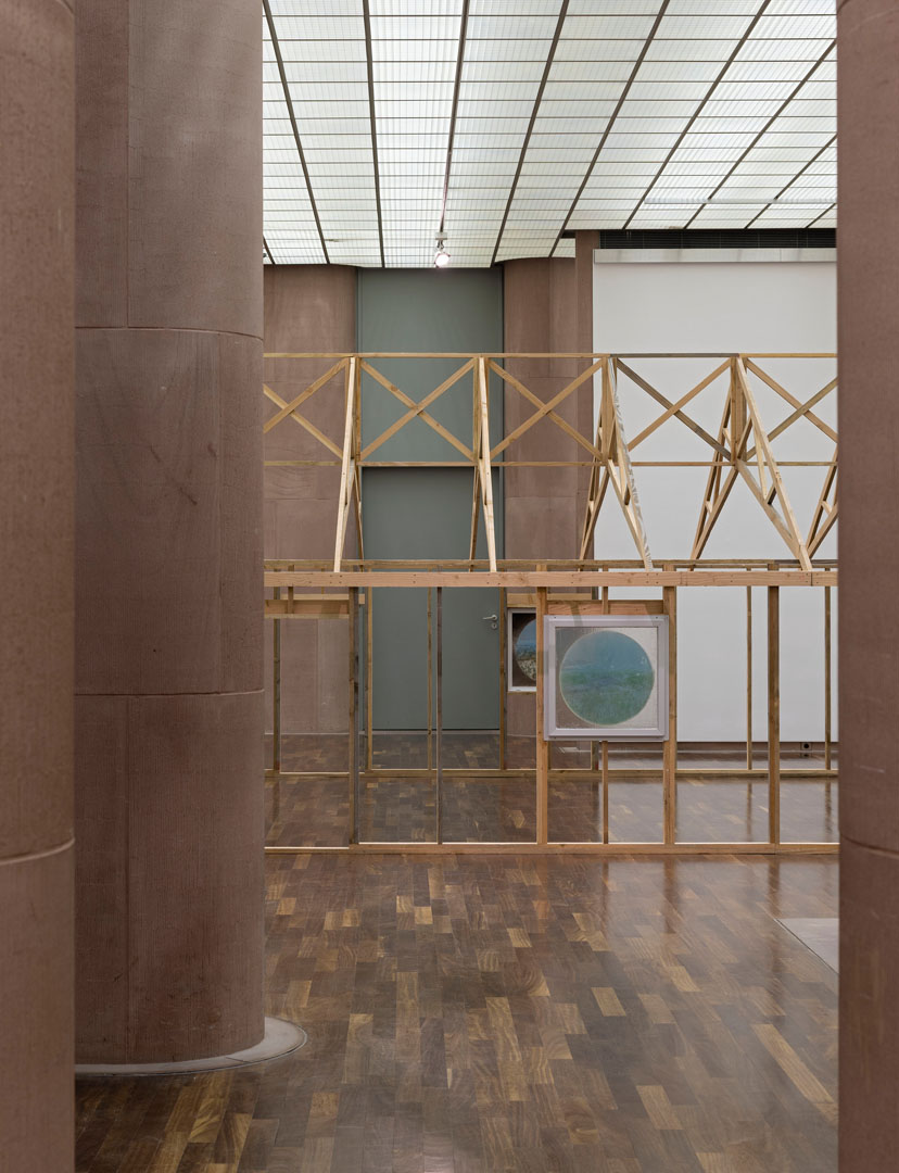 In einem Ausstellungsraum der Kunsthalle steht auf dem Parkettboden eine Hausstruktur. Es wirkt wie ein Rohbau aus Holz. Das Ständerwerk steht, nur die Wände und die Dacheindeckung fehlen. Die Fenster sind eingebaut: Es sind quadratische, in Aluminium gefasste Glasscheiben, die mit runden Motiven bemalt sind.