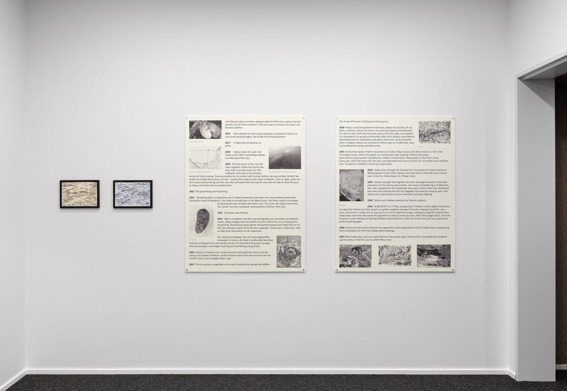 Auf einer weißen Wand zwei große Plakate mit viel Text und einigen Fotos in Schwarzweiß. Links daneben zwei kleine Tuschezeichnungen.