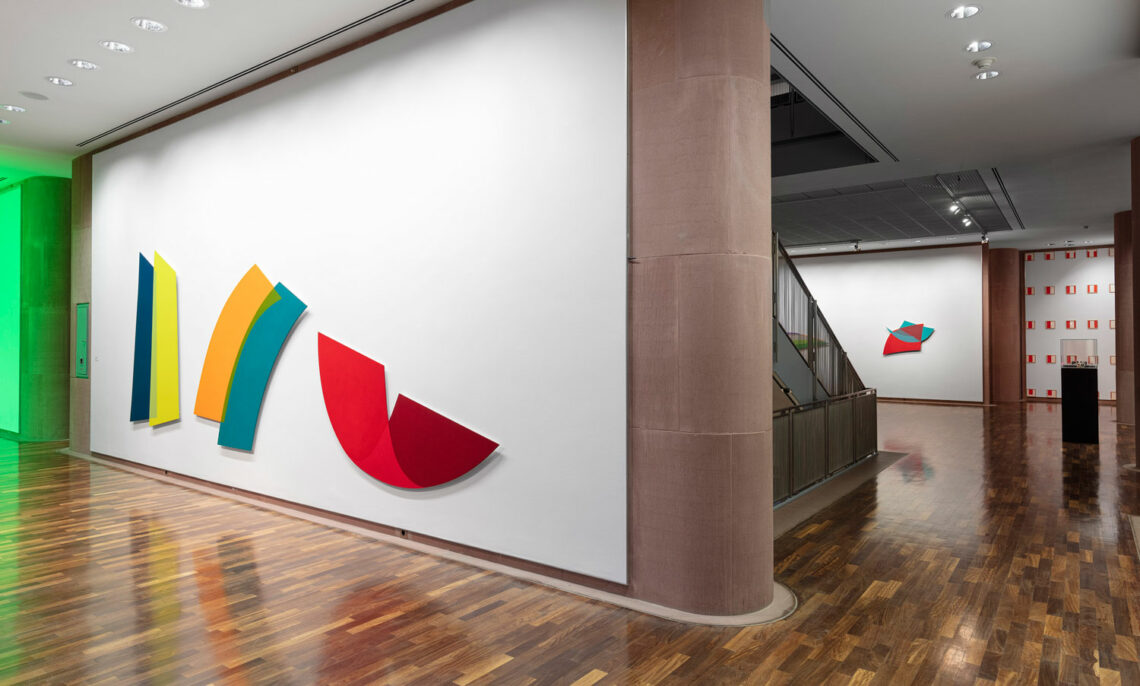 Several exhibition rooms in the Kunsthalle. In the foreground, curved colored rectangular shapes on a white wall. Further back, more works in different geometric shapes.