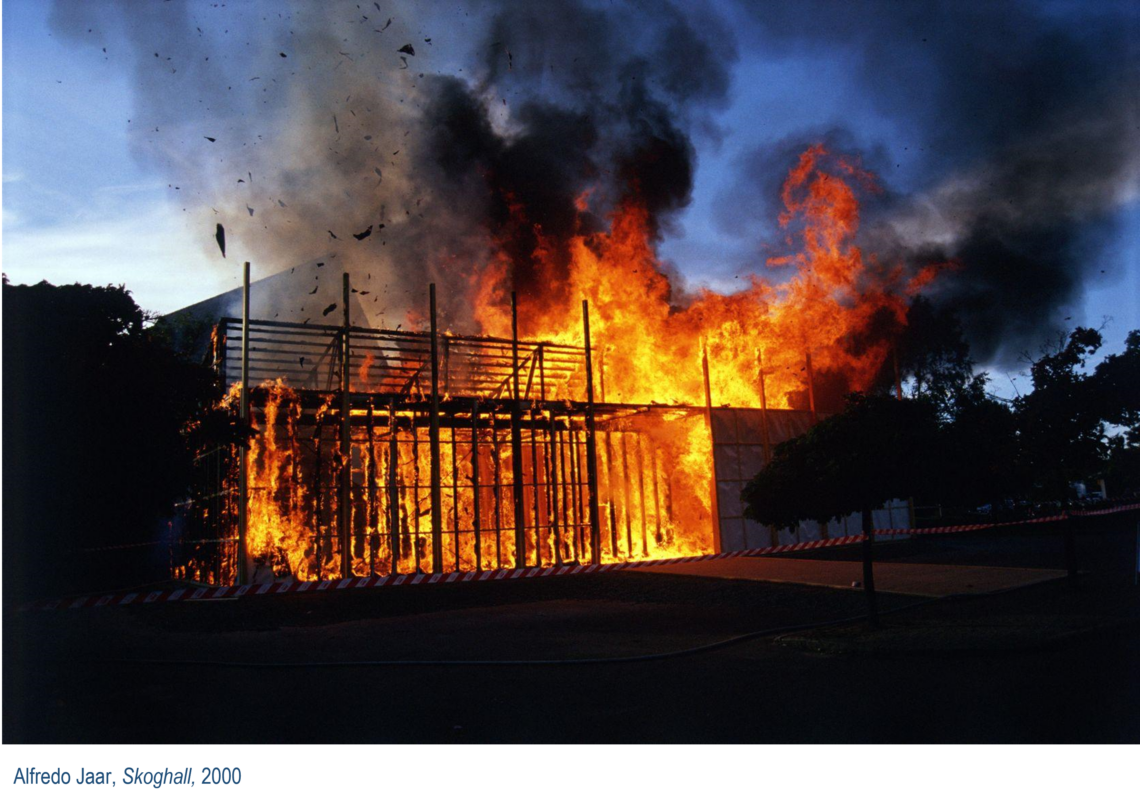 A large fire at dusk. It eats its way through a construction of wooden slats that form a building.